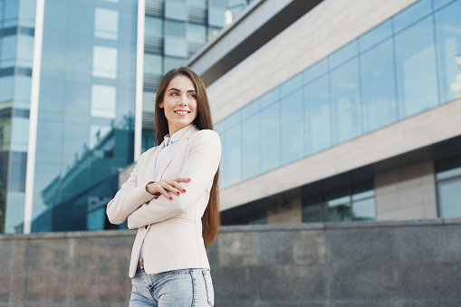 Portrait of thougtful confident caucasian businesswoman against modern glass office center background. Pensive young woman executive outdoors.