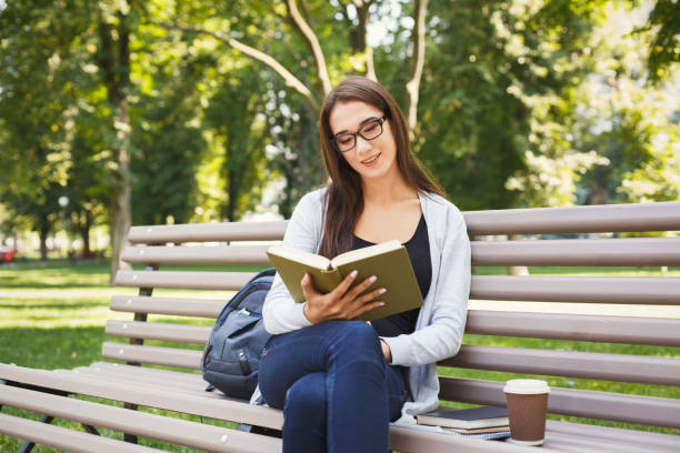 istock Young woman reading book in park copy space 909084314