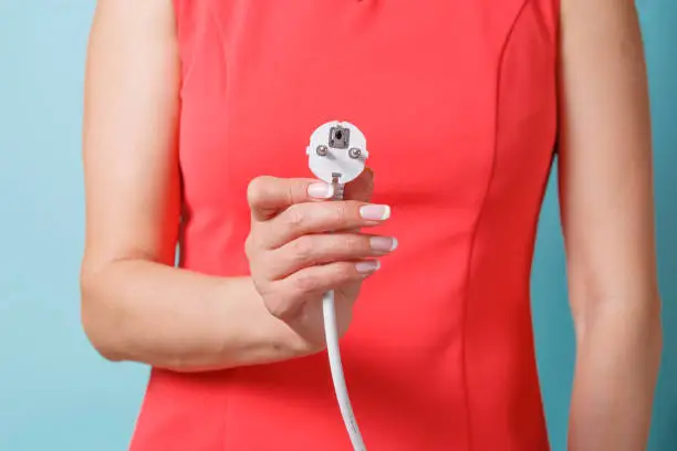 A woman in a red blouse holds an electric plug in her hand.
