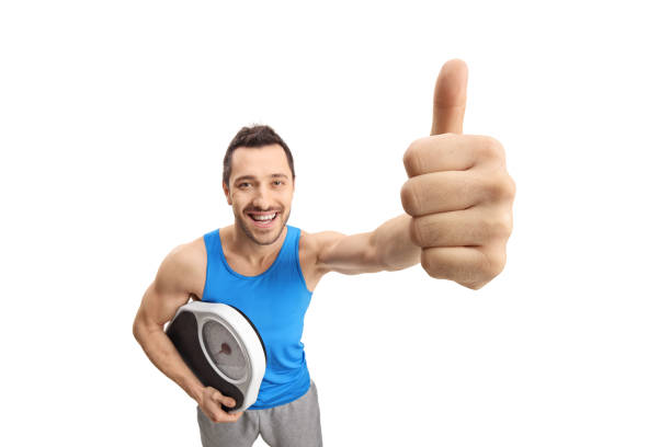 young man in sportswear holding a weight scale and making a thumb up gesture - human hand hand sign measuring scale imagens e fotografias de stock