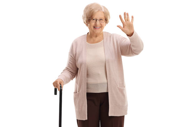 istock Elderly woman with a cane waving at the camera 909085788