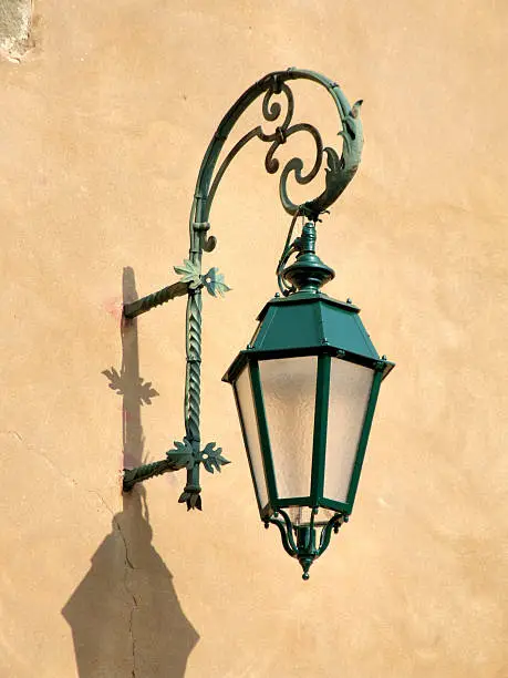 A green street lamp on a yellow wall.