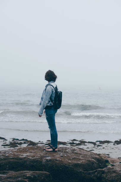 istock Woman with backpack walking on the beach in overcast weather 909092736