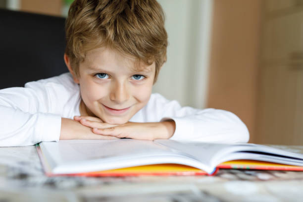 istock Little blonde school kid boy reading a book at home 909098014