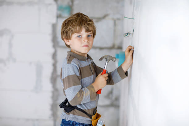 Little kid boy helping with toy tools on construction site. Funny child of 6 years having fun on building new family home. Kid with nails and hammer helping father to renovate old house