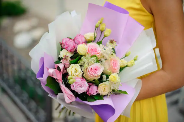 Elegant woman holds bouquet of different types of roses packed in white and purple wrapping-paper