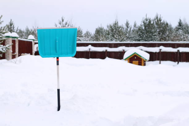 A shovel in a snowdrift on the background of small hut and forest.