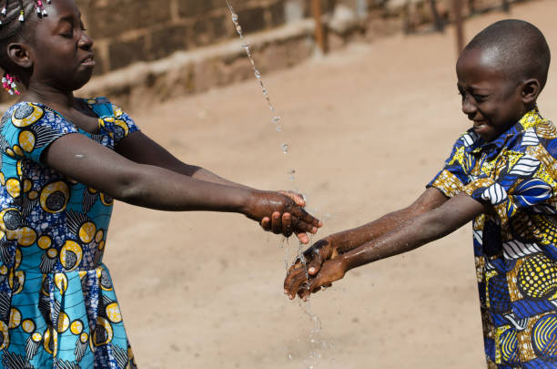 istock Two African Children Cleaning Hands Outdoors with Fresh Water 909126358