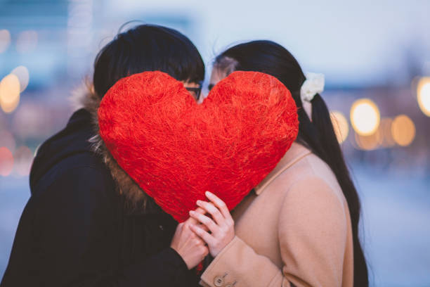 пара скрывается behing формы сердца и целовать друг друга - couple loving urban scene selective focus стоковые фото и изображения