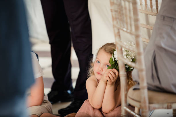 Little Girl Watching People at a Wedding Little girl is sitting on the dancefloor by a table at a wedding. She is watching the bride and groom share their first dance. flower girl stock pictures, royalty-free photos & images