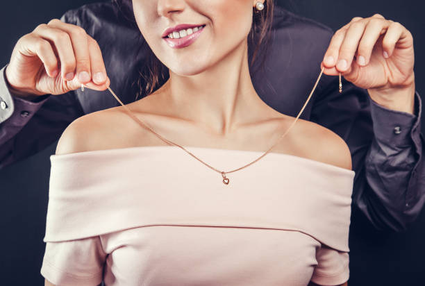 Man helping his girlfriend to try on a golden necklace. Gift for Valentines day. Man helping his girlfriend to try on a golden necklace on black background. Gift for Valentines day. pendant stock pictures, royalty-free photos & images