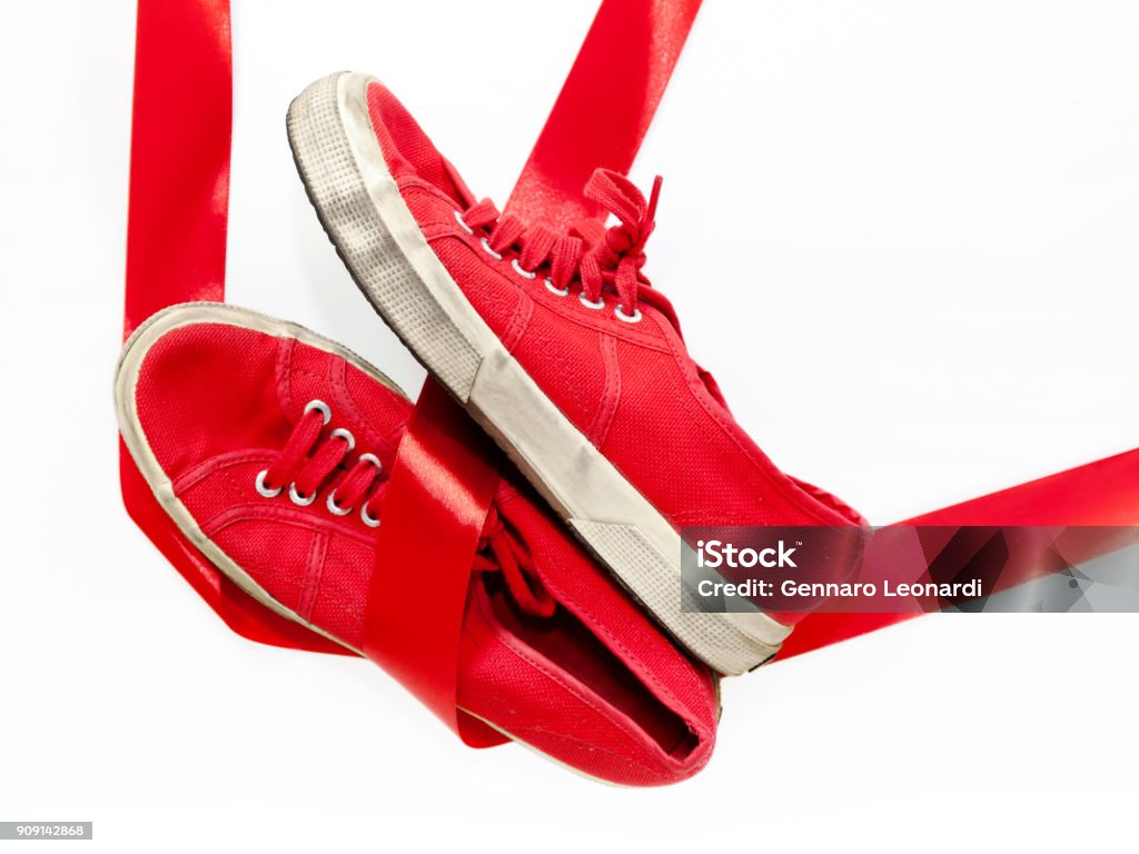 Red shoes, a symbol femicide. Illustrative editorial The model of red shoes for women, casual shoes on a white floor and joined by a red ribbon, which is the common thread that unites them: violence against women, symbolized by red shoes. Abuse Stock Photo