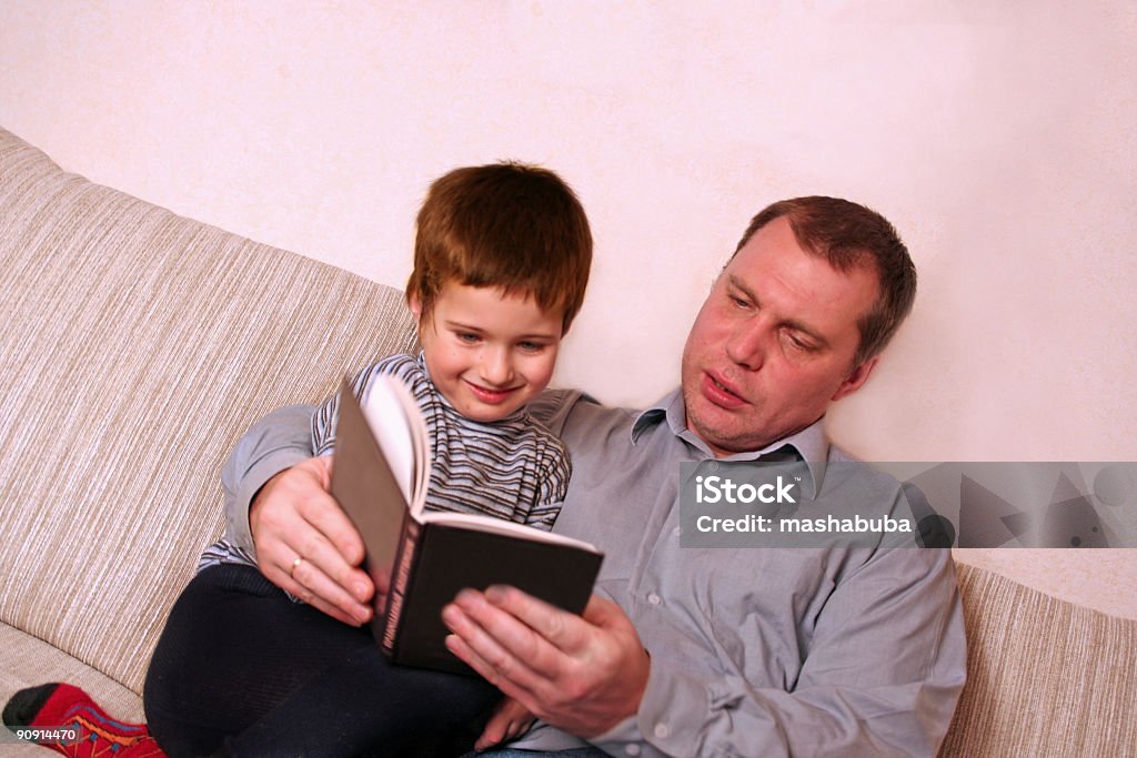 Padre con hijo se lea un libro en el sofá - Foto de stock de Acogedor libre de derechos