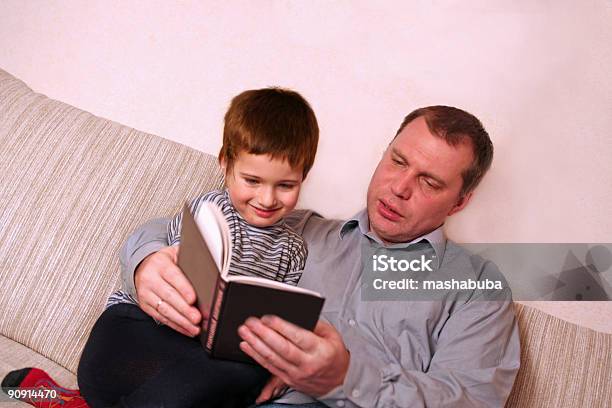 Padre Con Hijo Se Lea Un Libro En El Sofá Foto de stock y más banco de imágenes de Acogedor - Acogedor, Adulto, Alegre