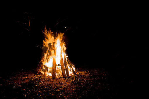 An outdoor bonfire with tall flames contained in boards shaped like a teepee