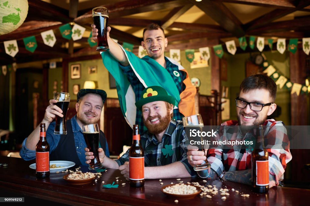 Happy friends enjoying beer party on St Patrick day Optimistic young men showing pints of dark beer and looking at camera while visiting St Patrick day party Carnival - Celebration Event Stock Photo
