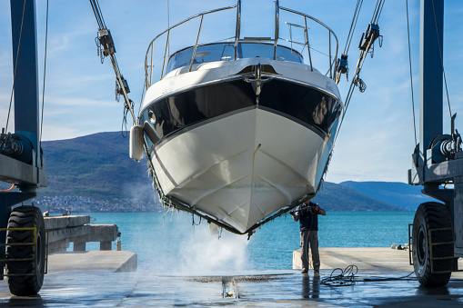Montenegro, Tivat, October 30 2017. Man is working at the Navar Boatyard. He is using a pressure washer to clean the bottom of the boat while it is in dry dock. He is removing barnacles from the prop and shaft. Boats need routine cleaning and maintenance.