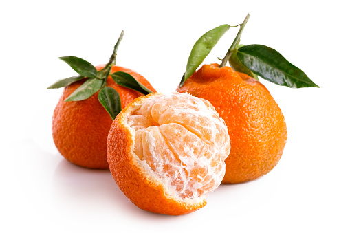 fresh oranges and some cut ones in a ceramic bowl on a white background