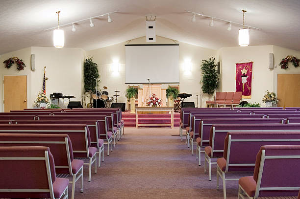 Church interior with pews and lights The interior of a church is shown. There is a pulpit and a screen in front of the rows of mauve-colored pews. place of worship stock pictures, royalty-free photos & images