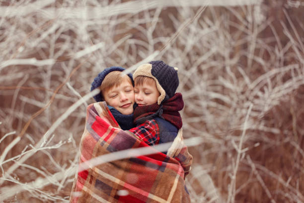 two brothers hugging each other covered with a warm blanket on a winter day