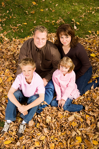 Vertical image of a beautiful young family sitting in a pile of leaves.