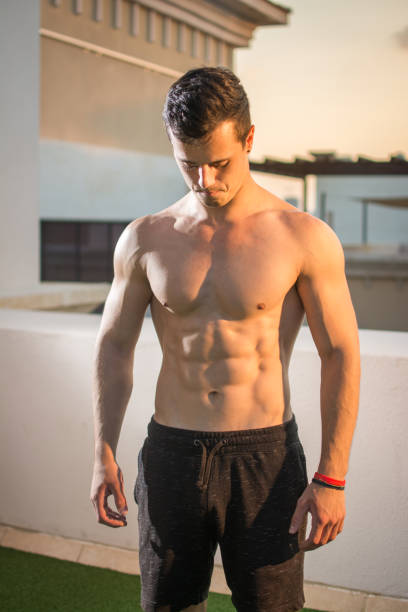 istock Bare-chested handsome muscular man in shorts standing outdoors and looking down. 909187212