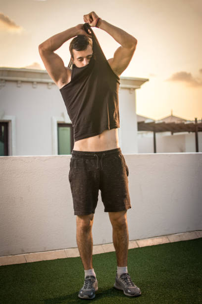 istock Handsome man taking off shirt outdoors. 909187494