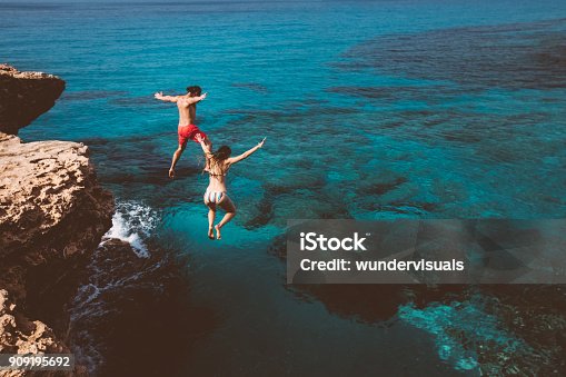 istock Young brave divers couple jumping off cliff into ocean 909195692