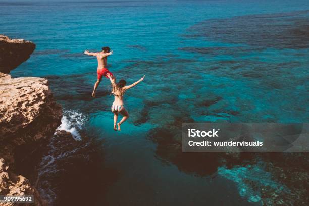 Young Brave Divers Couple Jumping Off Cliff Into Ocean Stock Photo - Download Image Now