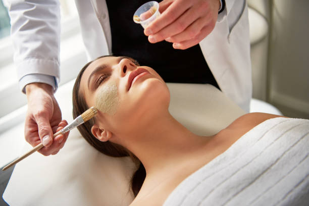 istock Woman lying with eyes closed while beautician putting mask 909195780