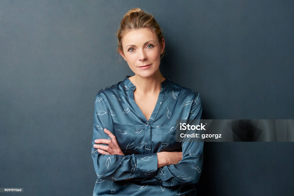 Beautiful woman portrait Studio shot of a smiling attractive middle aged woman standing with arms crossed at dark background. Women Stock Photo
