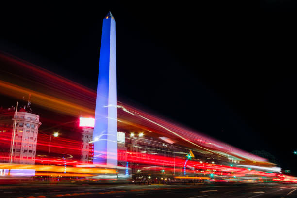 Night traffic of cars in the 9 de Julio Avenue next to the obelisk illuminated of blue. stock photo