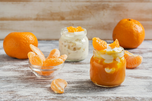 Yogurt in small jars with mandarin slices on a wooden white table