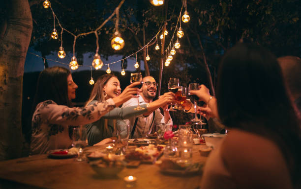 Friends toasting with wine and beer at rustic dinner party Happy young friends having fun and toasting around mediterranean dinner party table in Italian countryside garden party stock pictures, royalty-free photos & images