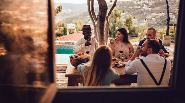 Young multi-ethnic friends and couples having lunch at village house Young multi-ethnic friends having fun eating and drinking at rustic mediterranean village countryside cottage restaurant rich black men pictures stock pictures, royalty-free photos & images