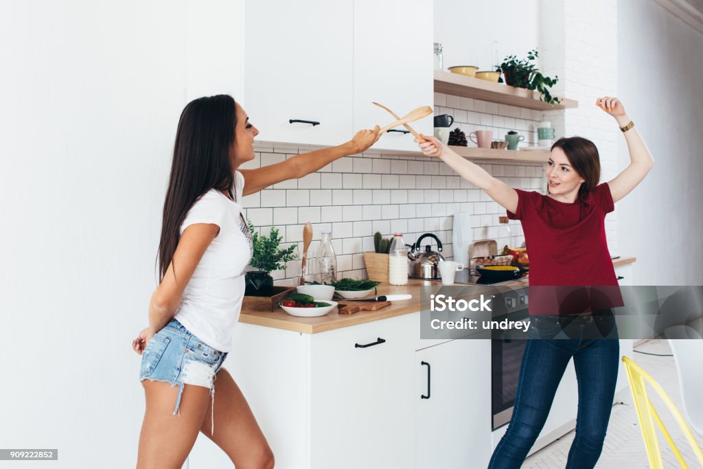 Two woman image that they are fighting on swords by wooden spatulas in kitchen Two woman image that they are fighting on swords by wooden spatulas in kitchen. Domestic Room Stock Photo