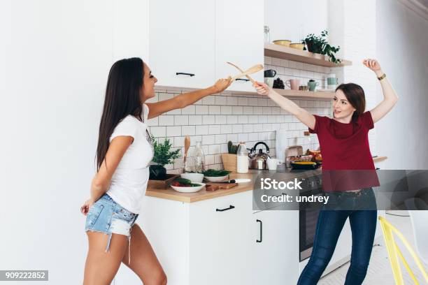 Two Woman Image That They Are Fighting On Swords By Wooden Spatulas In Kitchen Stock Photo - Download Image Now