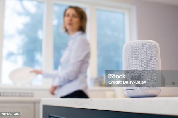 Woman In Kitchen Asking Digital Assistant Whilst Washing Up Stock Photo - Download Image Now