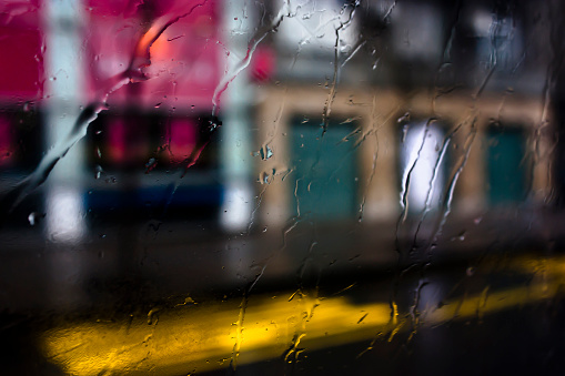 Blurry abstract rainy day, empty city street through bus window glass with raindrops