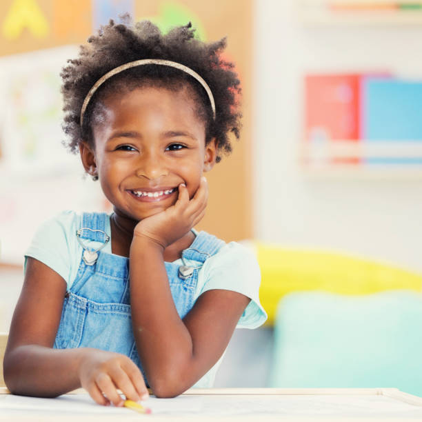 Portrait of adorable preschooler in her classroom Beautiful preschool girl smiles while at school. She is smiling cheerfully at the camera. children only stock pictures, royalty-free photos & images