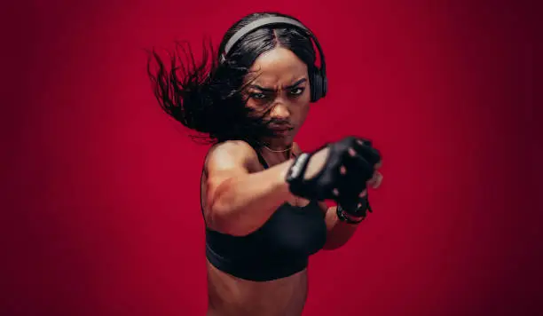 Boxer practicing her punches in a studio. African female boxer practicing boxing against red background.