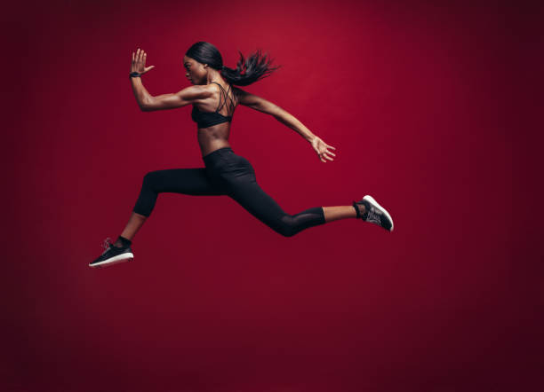 Female athlete running and jumping Female athlete running and jumping. Side view shot of healthy african woman working out against red background. carpet runner stock pictures, royalty-free photos & images