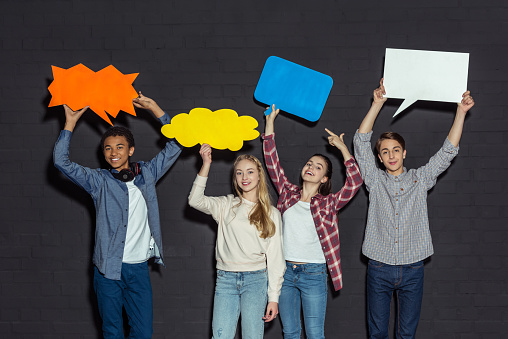 group of teenagers holding blank speech bubbles over heads on black