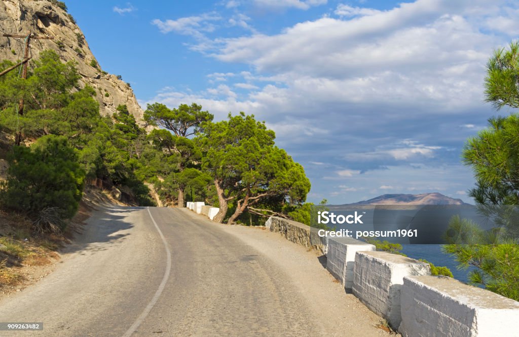 A mountain road along the seashore. A mountain road along the seashore. Sunny summer day. (The road Sudak - Novyy Svet, Crimea). Antiquities Stock Photo