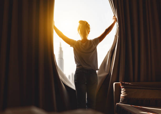 happy woman stretches and  opens curtains at window in morning - sunny apartment window sky imagens e fotografias de stock