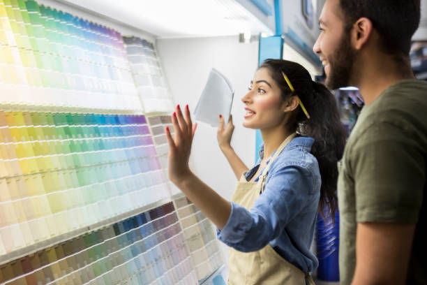 Paint store employee assists male customer Confident young female paint store employee shows a male customer paint samples. They are standing in front of a display of the samples. hardware store photos stock pictures, royalty-free photos & images