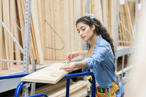 Home improvement warehouse employee measures board Female lumber yard employee carefully measures a wooden board. She is filling a customer's order. woman wearing tool belt stock pictures, royalty-free photos & images