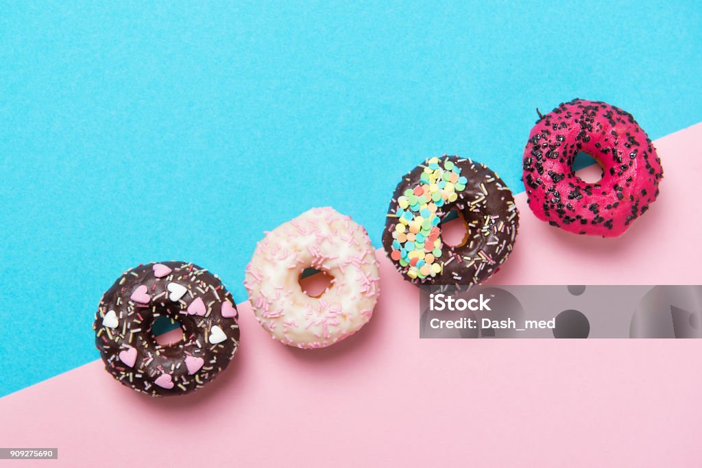 Assortiment de beignets colorés dans une rangée, minimalisme sur un fond bleu et rose, vue de dessus - Photo de Beignet libre de droits