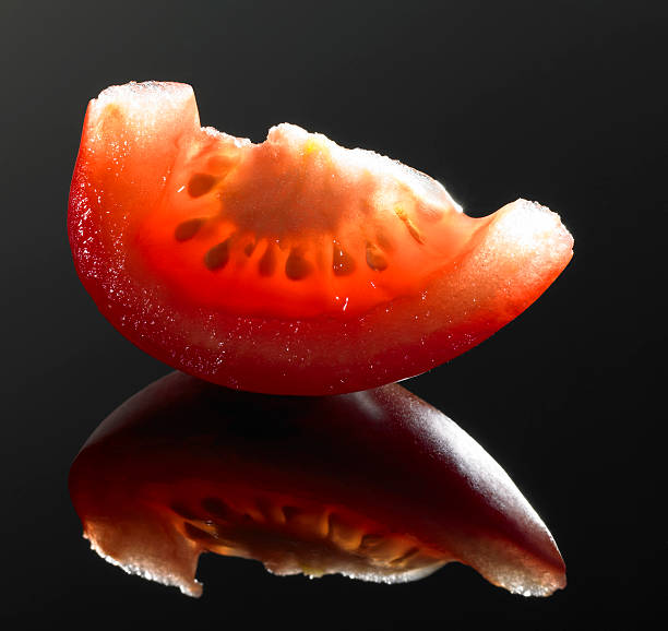 tomato cut studio shot of a sapful tomato cut in black reflective back vermehrung stock pictures, royalty-free photos & images