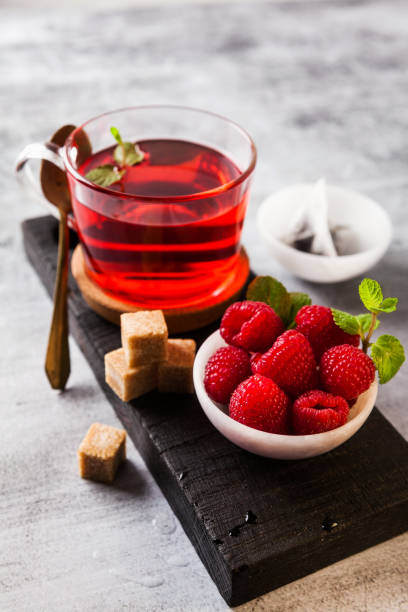 istock hot raspberry tea in transparent cup on a stone table. Fresh berries, cubes of cane sugar and a bag of tea 909291284